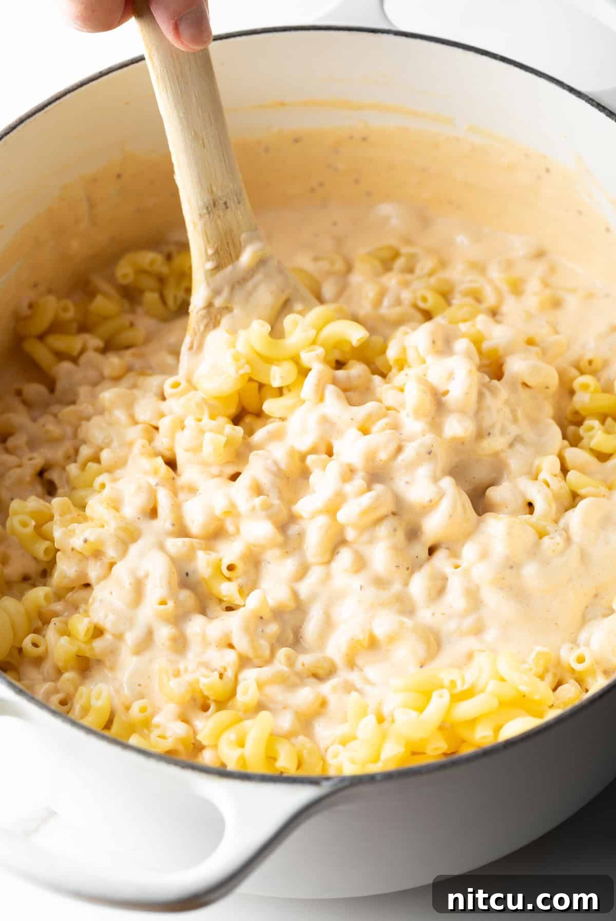 Macaroni pasta is being stirred into the cheese sauce for lobster mac and cheese.