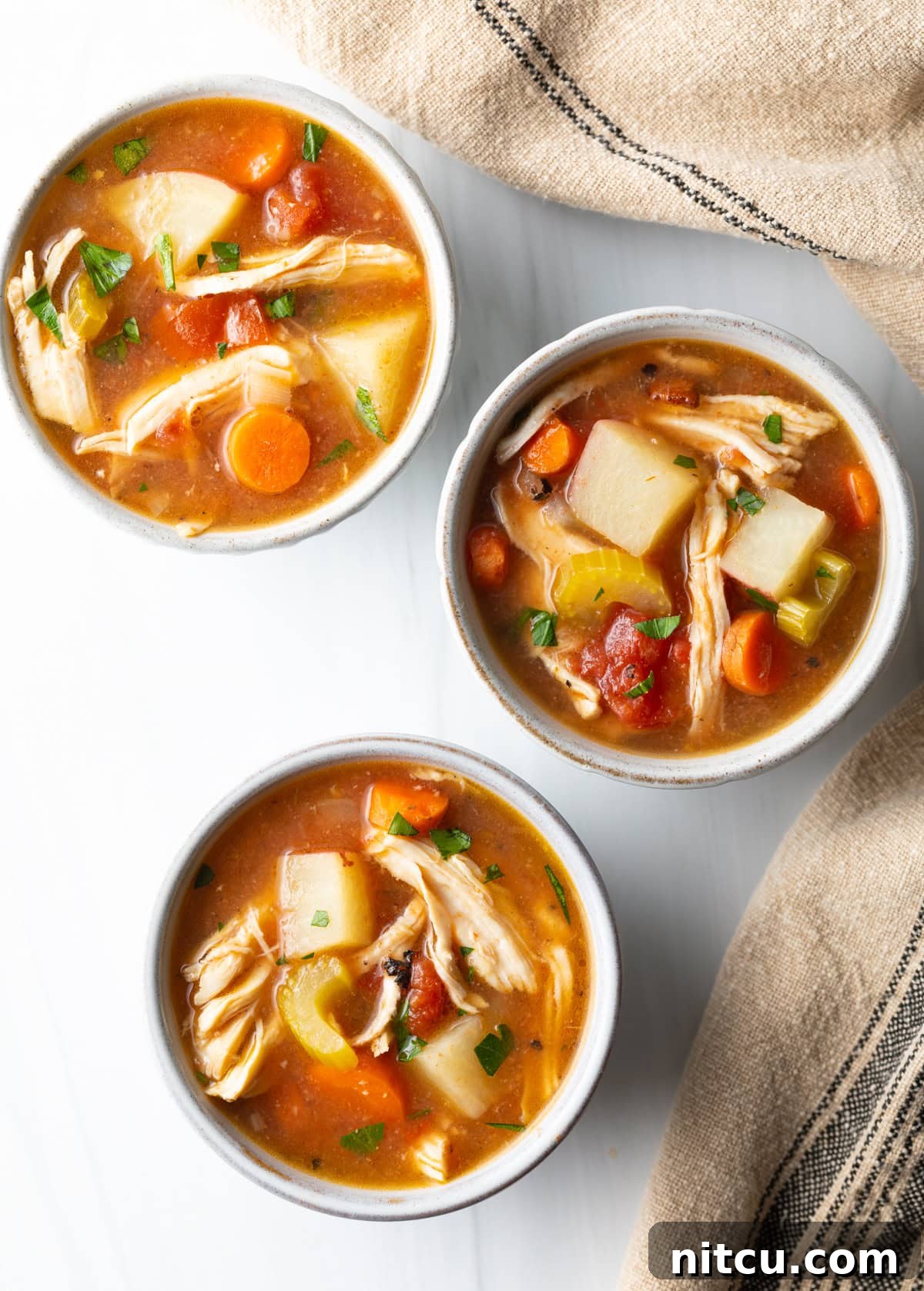 Top down view of 3 small white bowls of chicken stew with potatoes, carrots, and celery in a tomato broth.