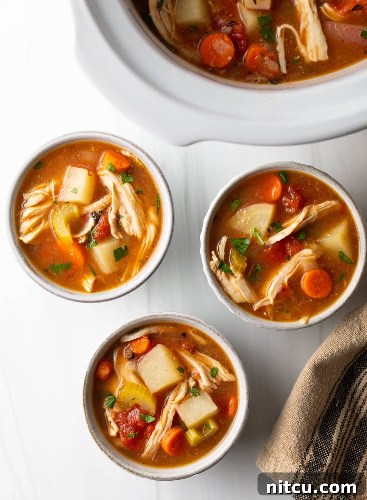 Top down view of 3 small white bowls of chicken stew with potatoes, carrots, and celery in a tomato broth.