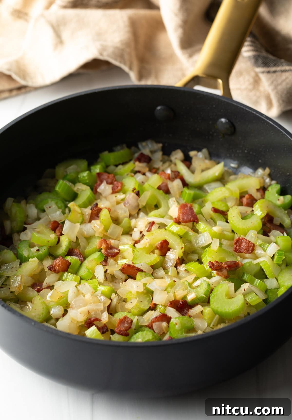 Sautéing diced bacon, celery and onions in a large black pan.