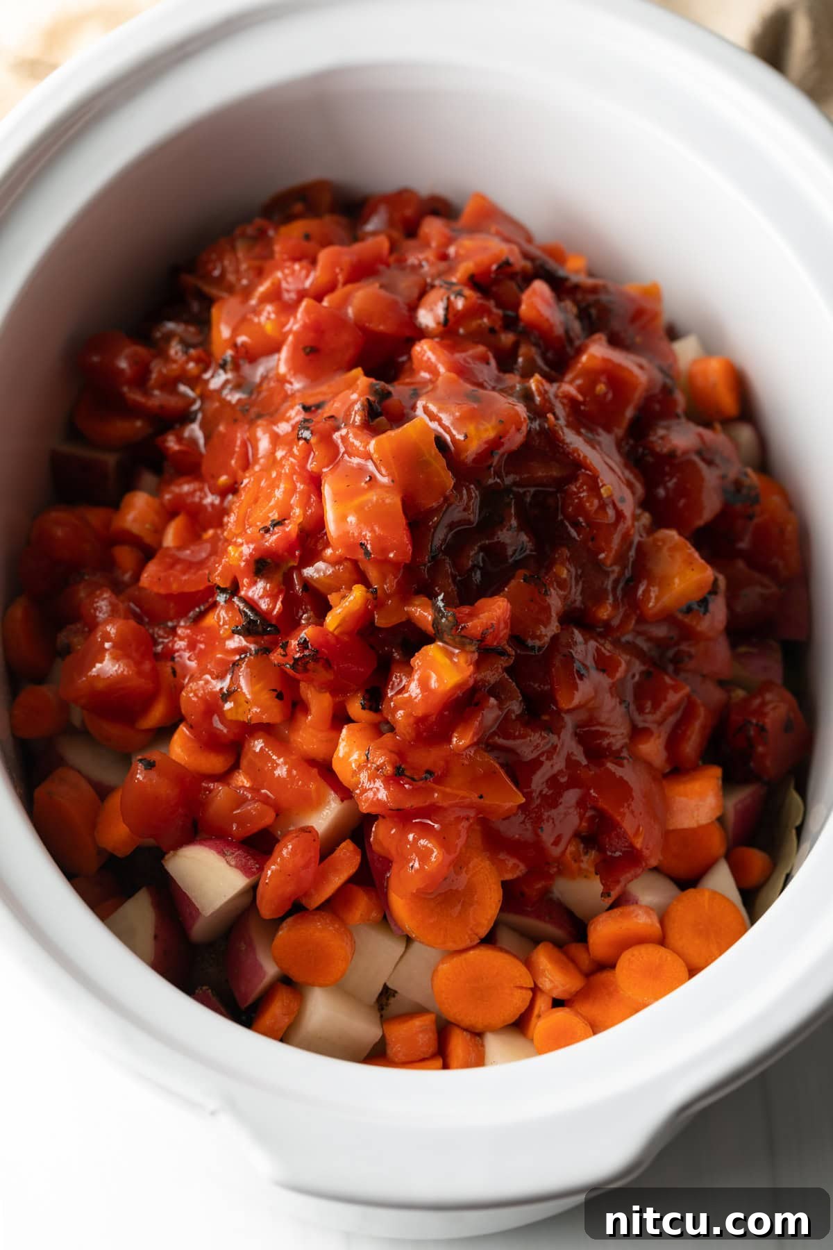 Canned diced tomatoes added onto the veggies in a white slow cooker.
