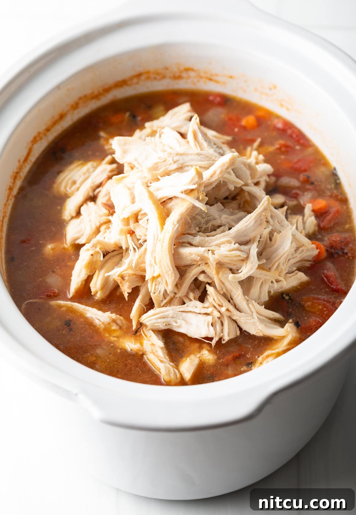Shredded chicken on top of a tomato soup base in a slow cooker.