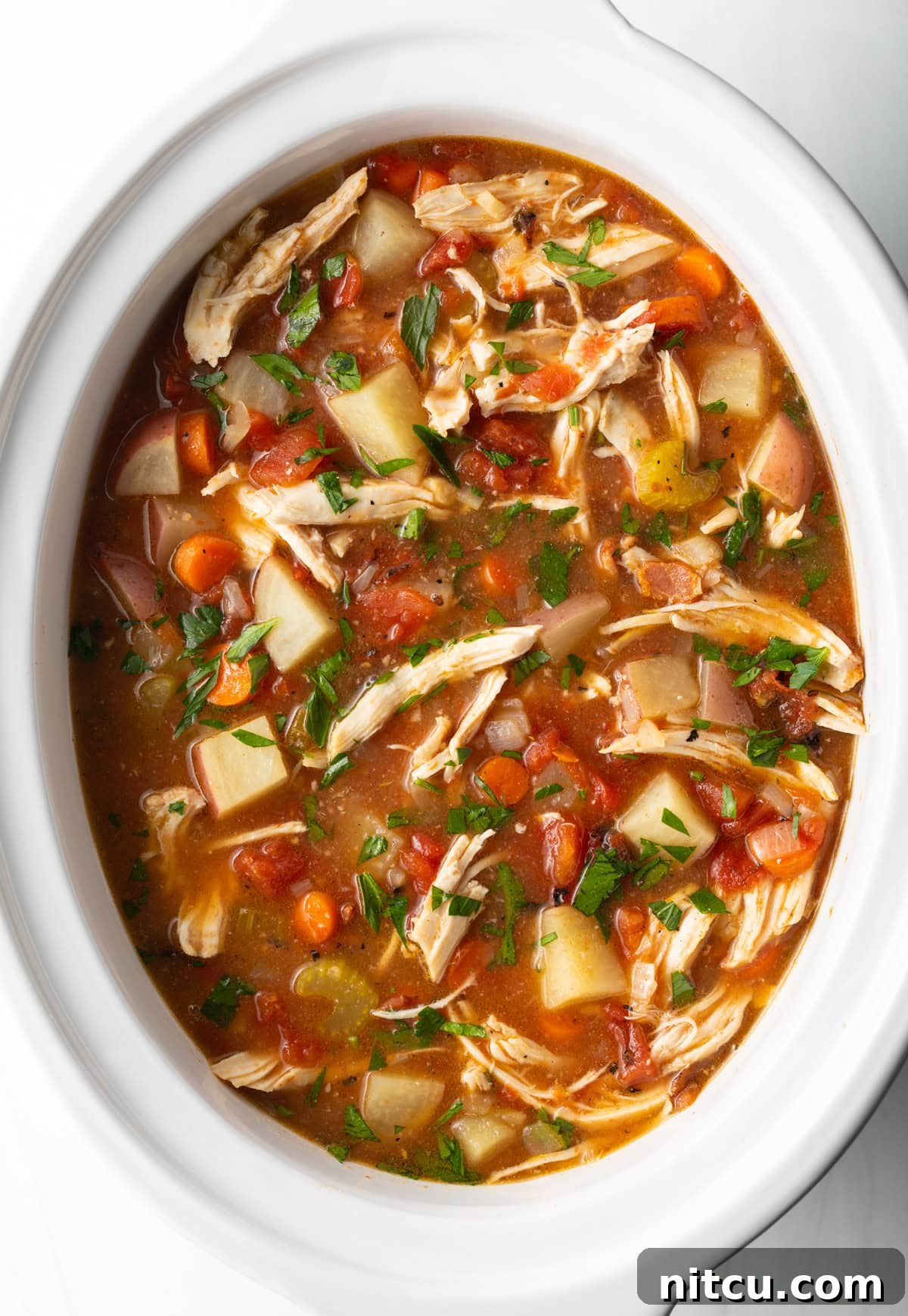 Healthy crock pot chicken stew in a white crock pot, ready for serving.