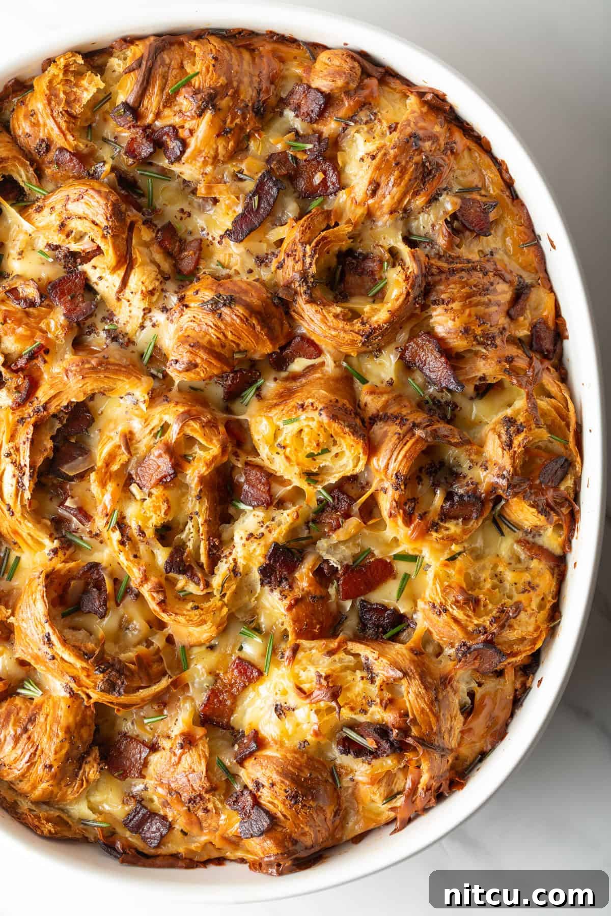 A perfectly baked croissant breakfast casserole recipe in a white baking dish, boasting a golden crust, just removed from the oven.