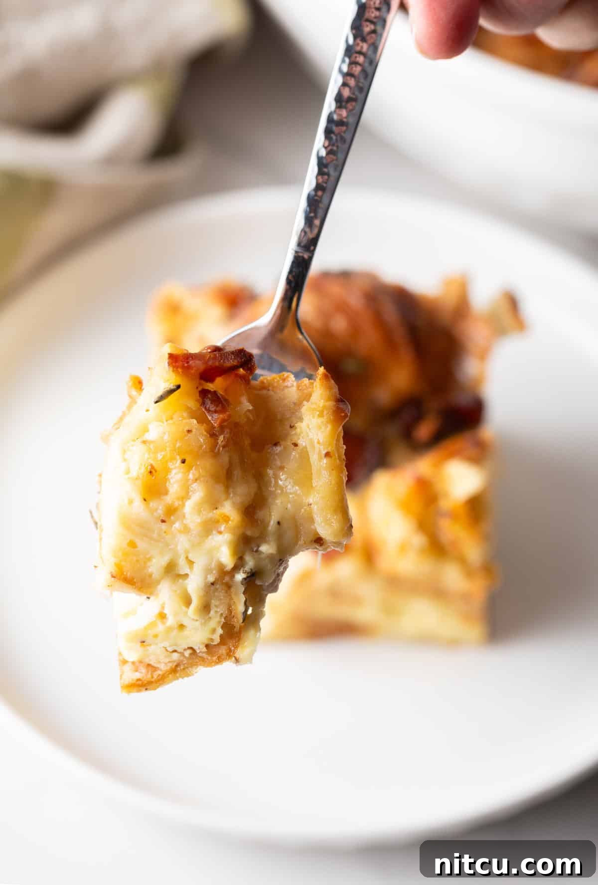A delicious forkful of golden-brown croissant casserole held up to the camera, inviting a taste.