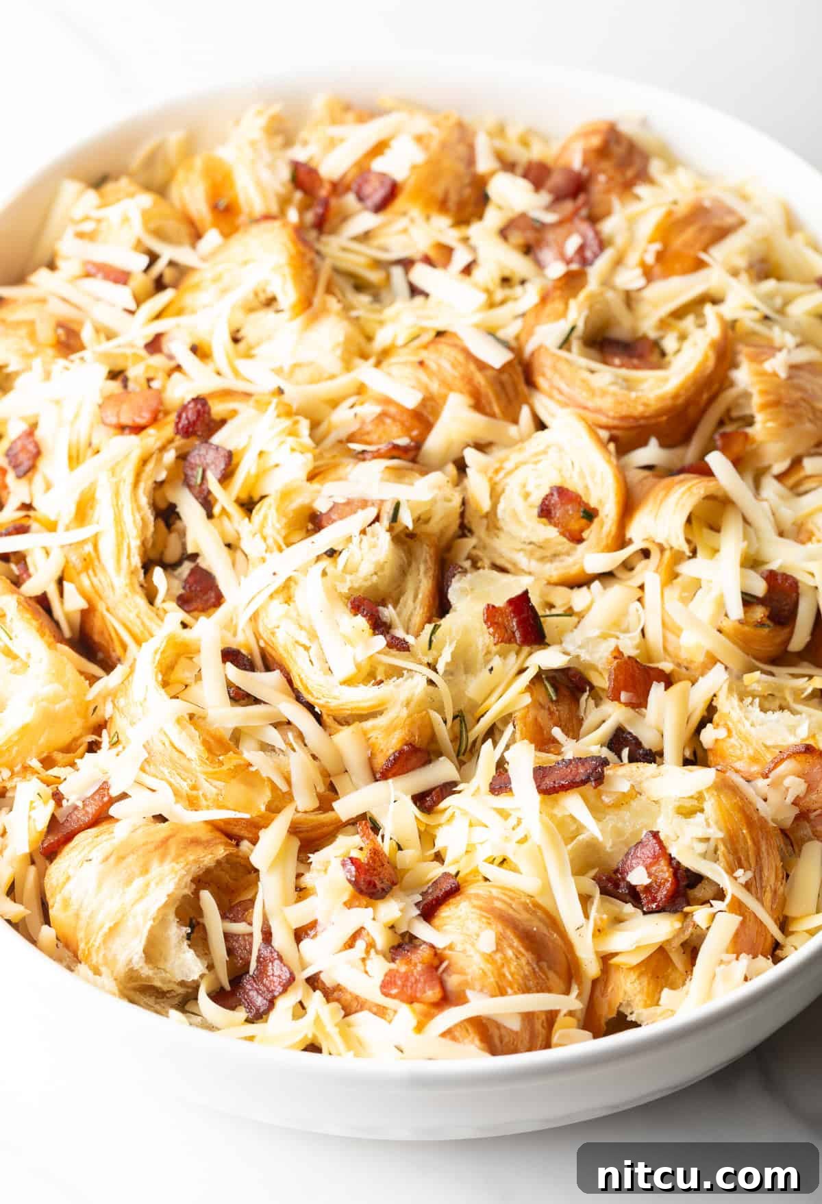 Shredded Gouda cheese generously sprinkled over the unbaked croissant breakfast casserole, ready for the egg mixture.