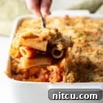 A serving of easy chicken parmesan casserole is being scooped out of a white baking dish.