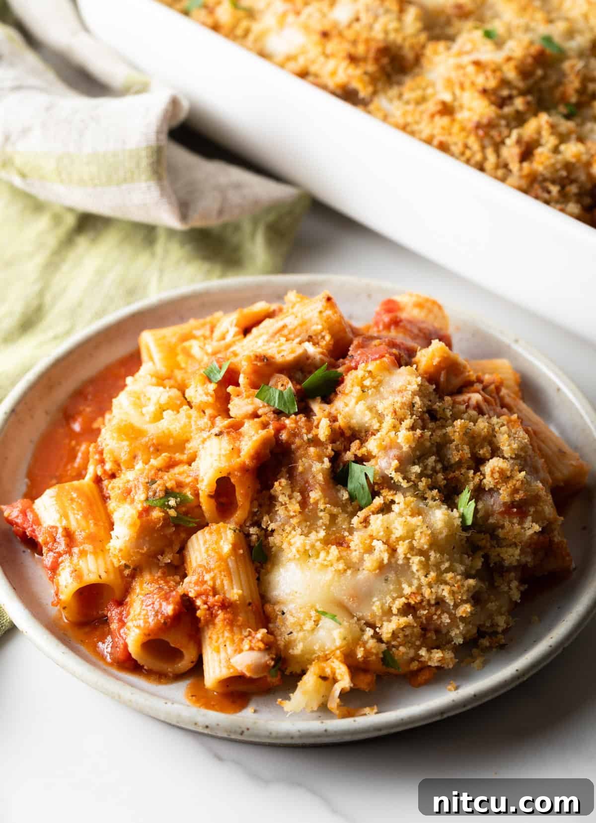 A generous helping of chicken parmesan casserole served on a white plate, showcasing its rich sauce and cheesy topping.