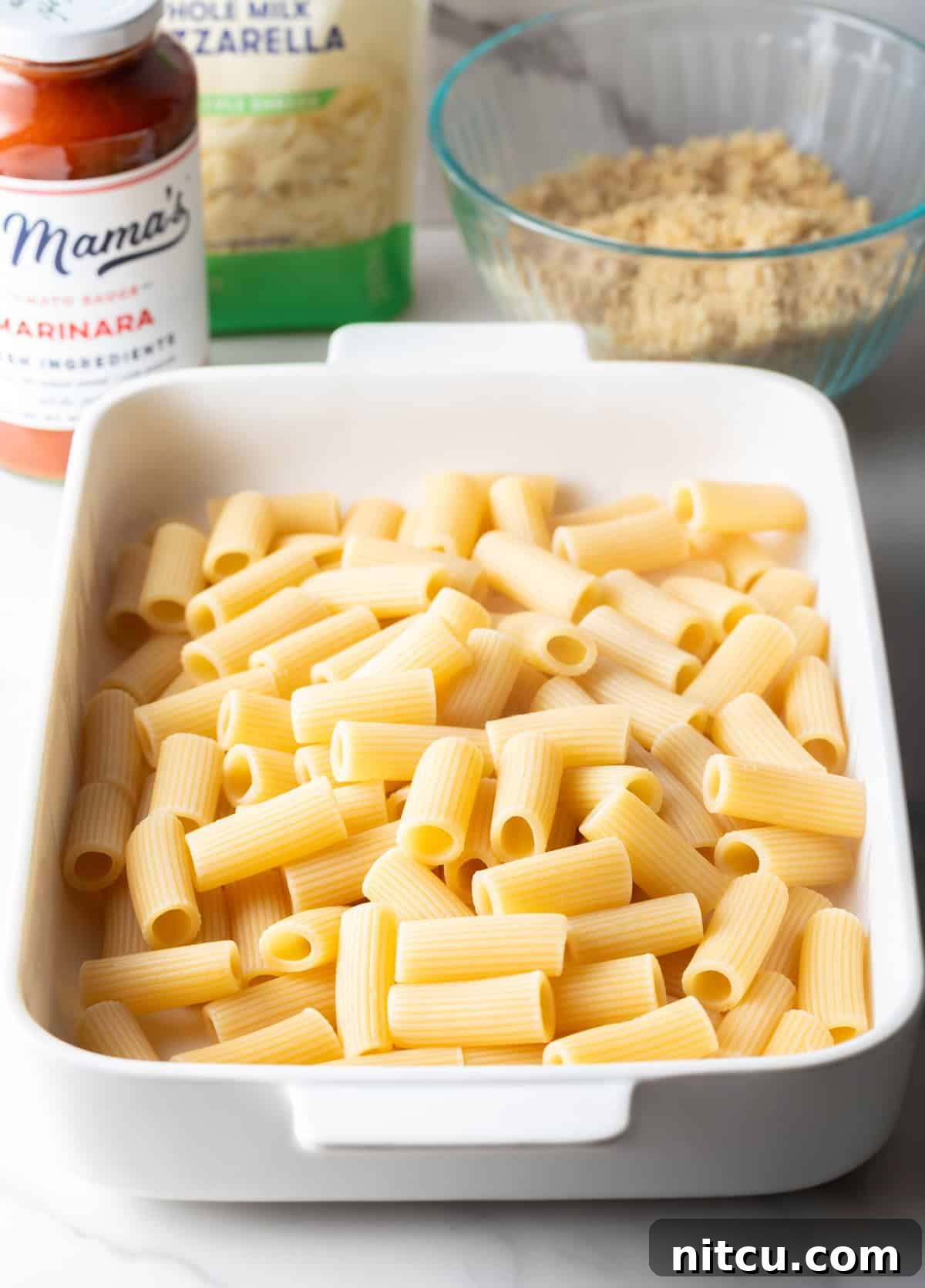 Cooked rigatoni pasta spread evenly in a white 9x13 inch baking dish.