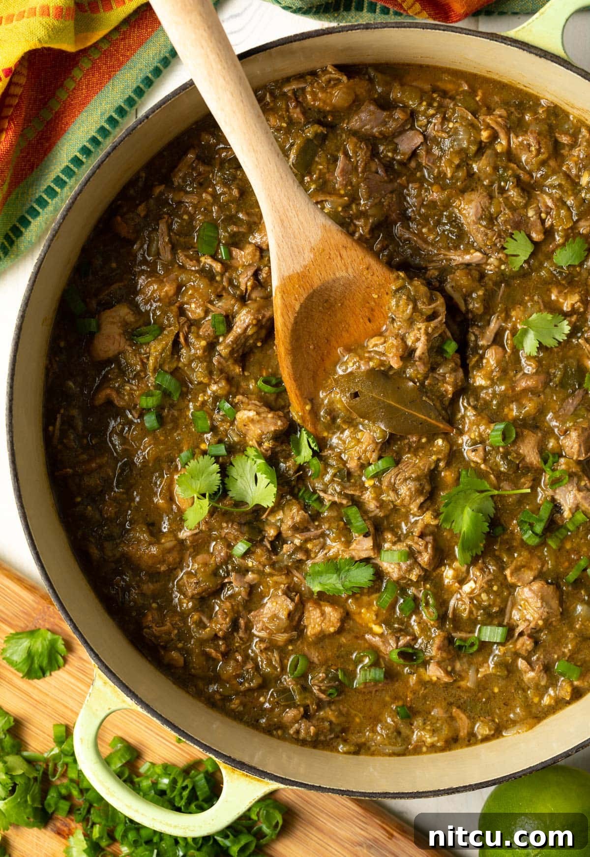 Dutch oven full of savory pork green chili with a wooden spoon, ready to be served.