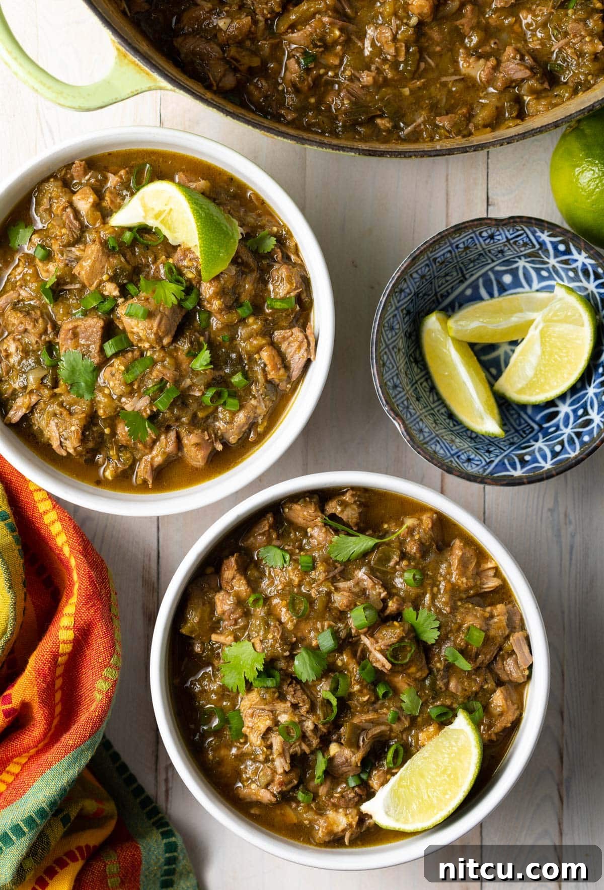 Two bowls of New Mexican green chile with fresh lime wedges on the side, ready for serving.