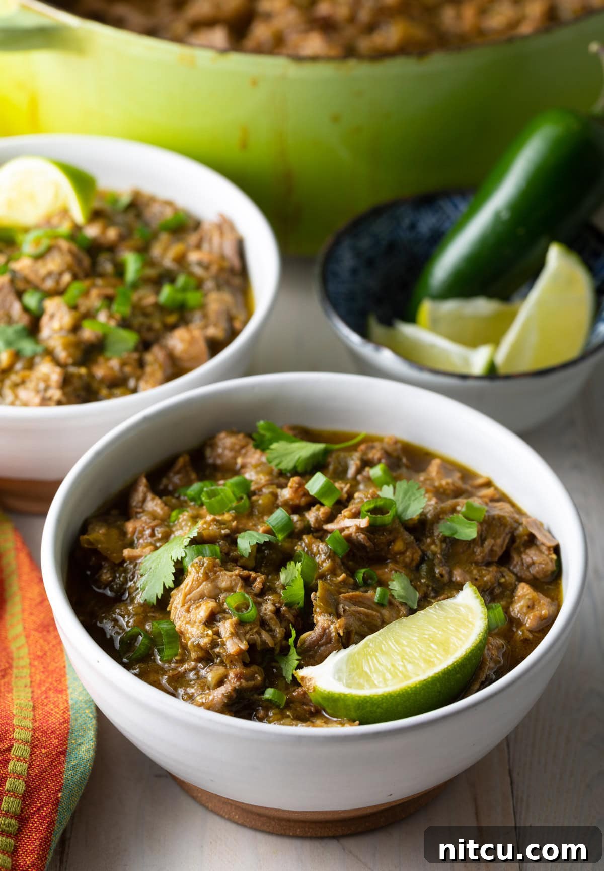 Two bowls of Green Chili (Chile Verde) adorned with fresh lime wedges, ready to be enjoyed.