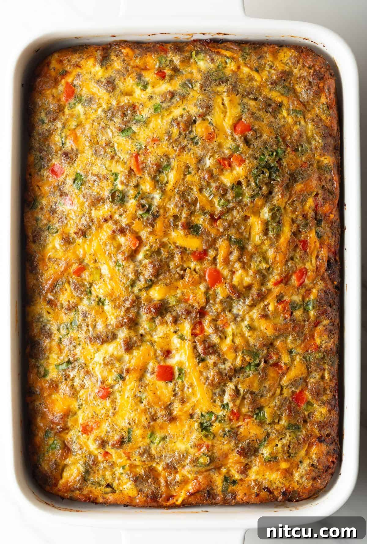 Top down view of a baked egg, sausage, and cheese casserole in a white rectangle dish.