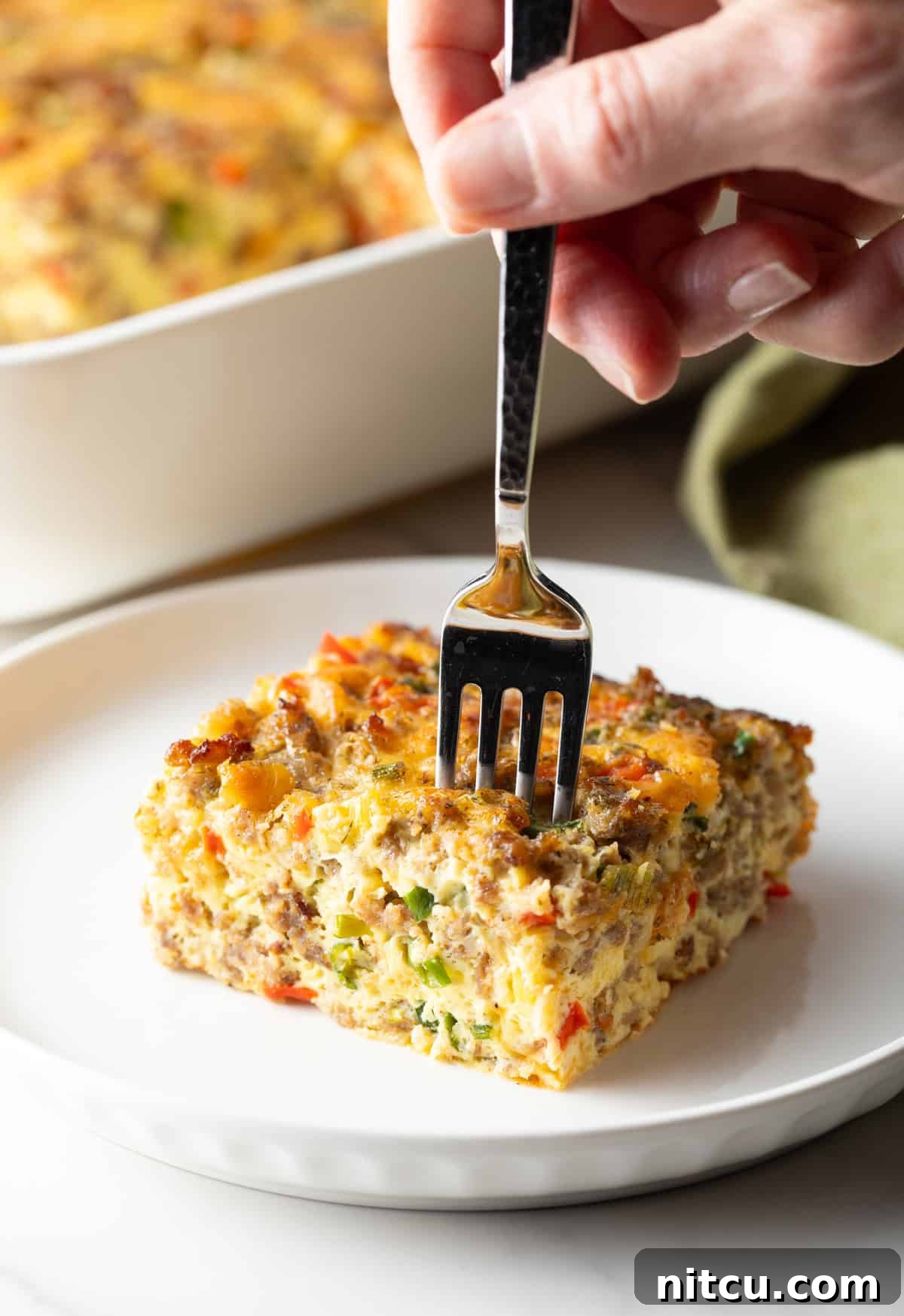 Fork taking a section from a square of sausage breakfast casserole on a white plate.