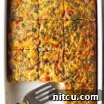 Pan of egg casserole with sausage and vegetables. A spatula is in the pan, with square portions of the casserole removed.
