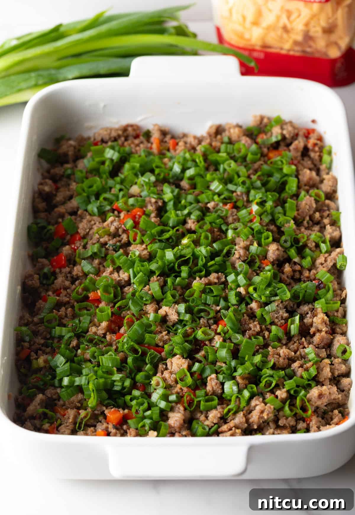 Cooked sausage and bell pepper mixture spread evenly in a white rectangle baking dish.