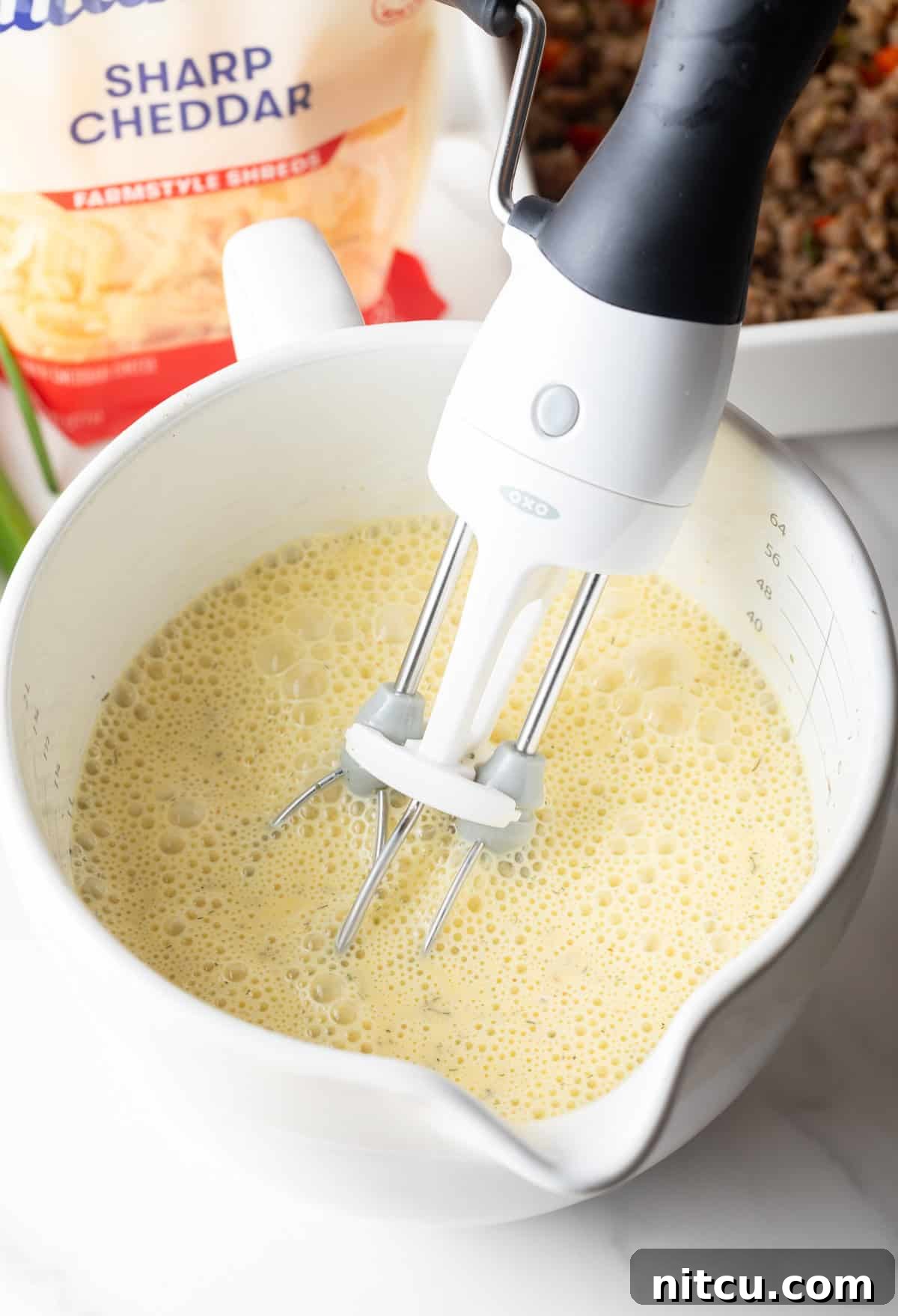 Hand mixer blending eggs and spices in a white measuring pitcher.