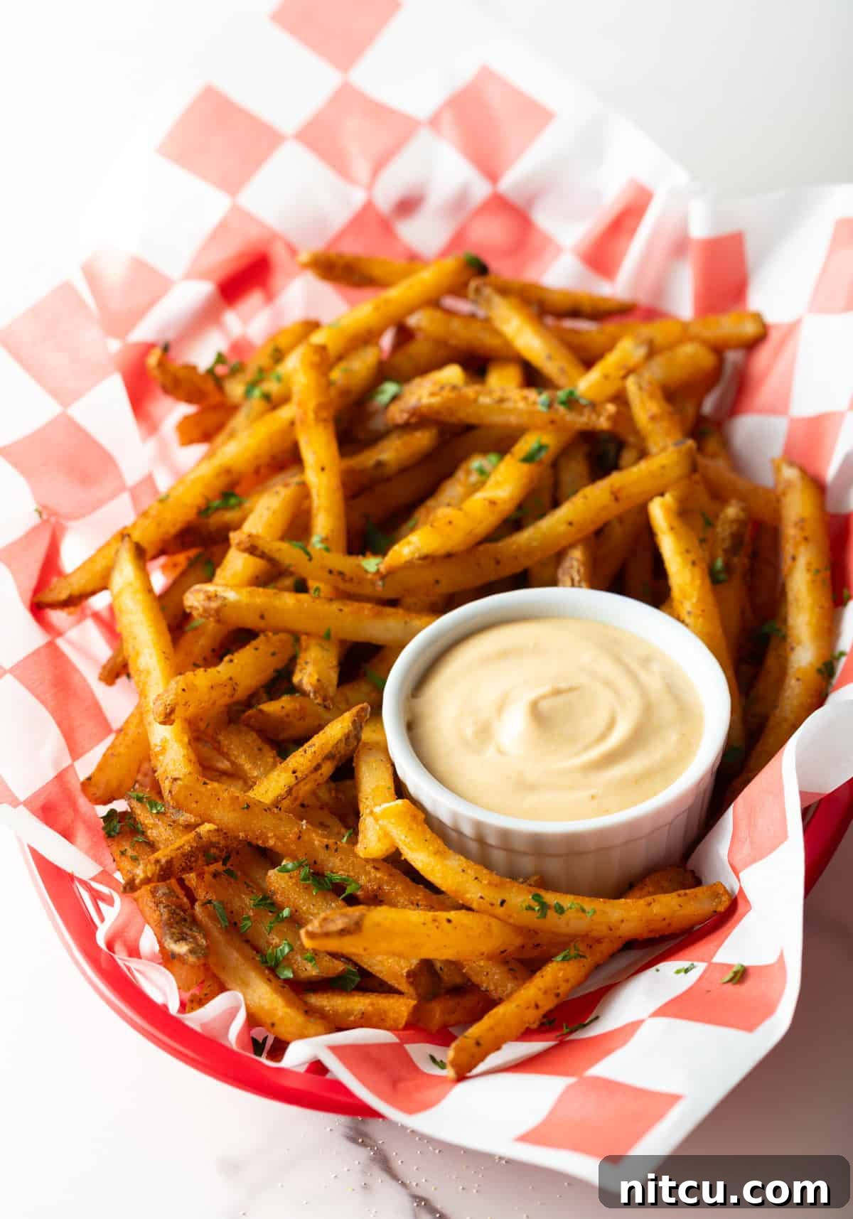 A paper-lined basket of French fries surrounding a white ramekin filled with homemade French fry sauce.