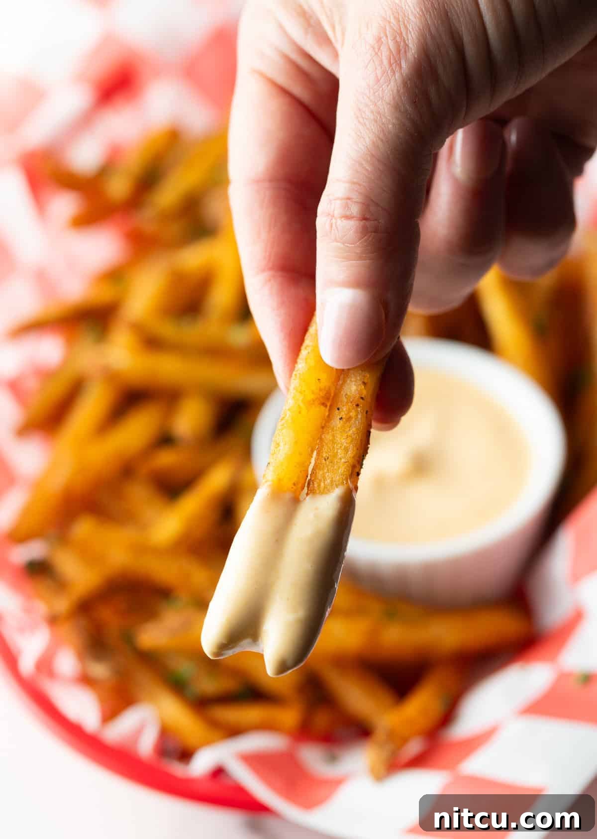 A hand holding two French fries that have been dipped in French fry dipping sauce.