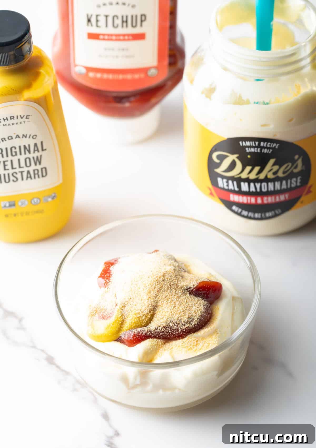 A glass bowl filled with mayonnaise, mustard, ketchup, and seasonings.
