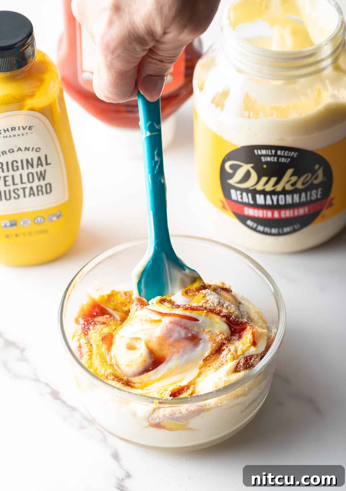 A spatula stirring French fry sauce ingredients in a glass bowl.