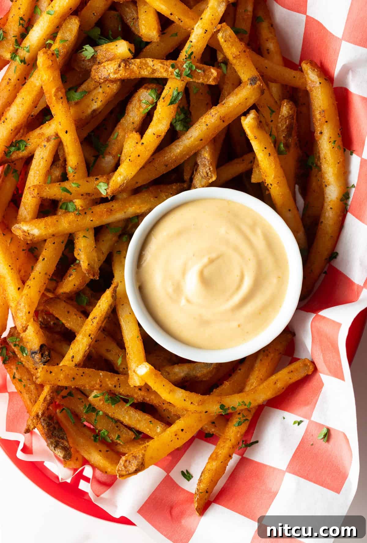 Overhead shot of a paper-lined basket of French fries surrounding a white ramekin filled with homemade French fry sauce.