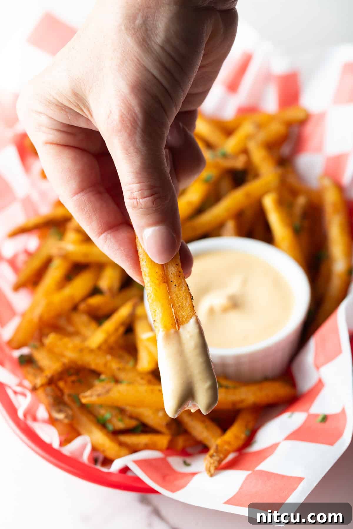 A hand holding two French fries that have been dipped in easy French fry dipping sauce.
