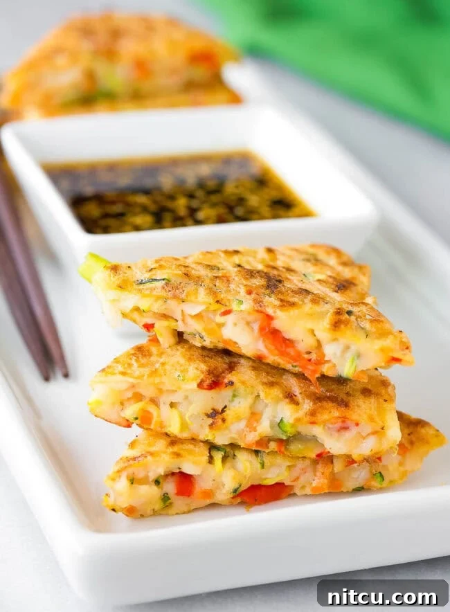 A close-up inside view of perfectly cooked Korean vegetable pancakes (Pajeon) arranged on a platter, showcasing the vibrant julienned vegetables embedded within the tender, savory batter.