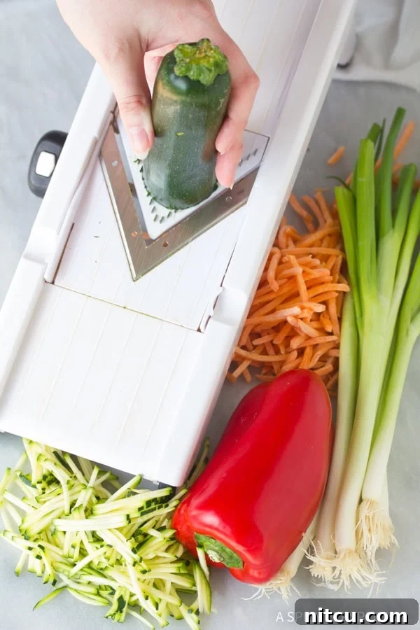 A hand is expertly using a mandolin slicer to prepare the fresh vegetables, ensuring thin, uniform strips perfect for Korean Pajun pancakes.