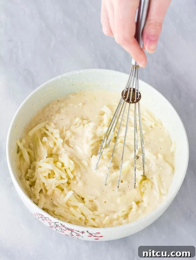 A light-colored, savory Korean pancake batter is being vigorously whisked in a large mixing bowl, creating a smooth and consistent base for the Pajeon.