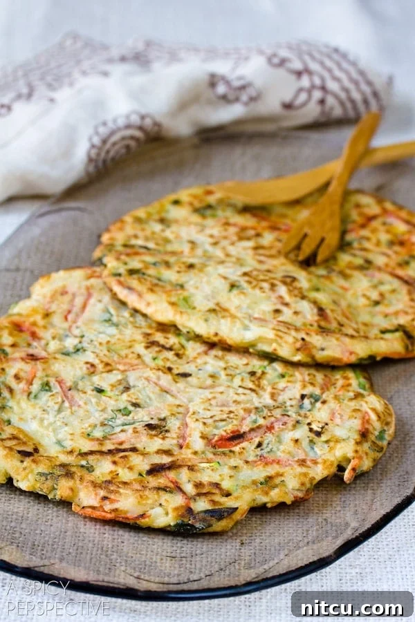 Two freshly fried Korean pancakes are presented side-by-side on a white plate, showcasing their perfect golden crust and inviting texture.