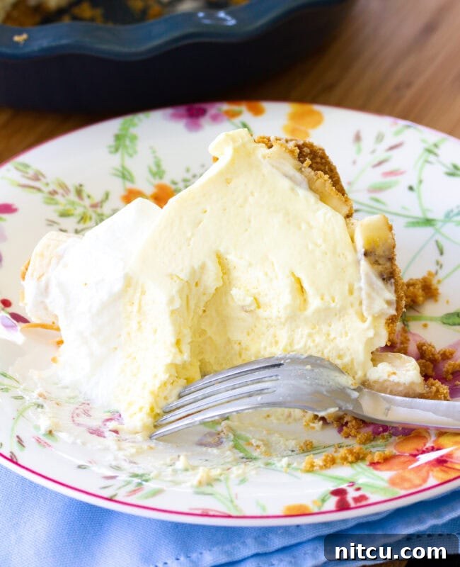 A slice of banana cream pie on a plate, with a fork beside it, and a larger portion of the pie missing from the pan.