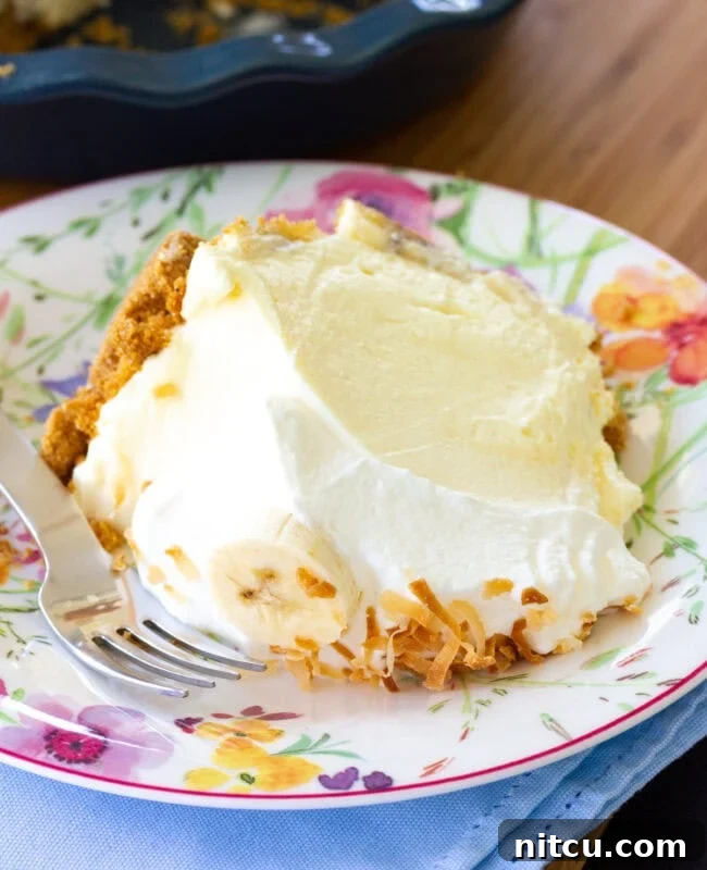 A close-up slice of banana cream pie on a white plate, highlighting the layers of crust, bananas, creamy filling, and whipped topping.