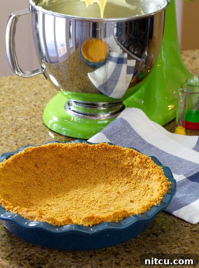 Graham Cracker Crust mixture in a pie dish, ready to be pressed, with a stand mixer in the background.