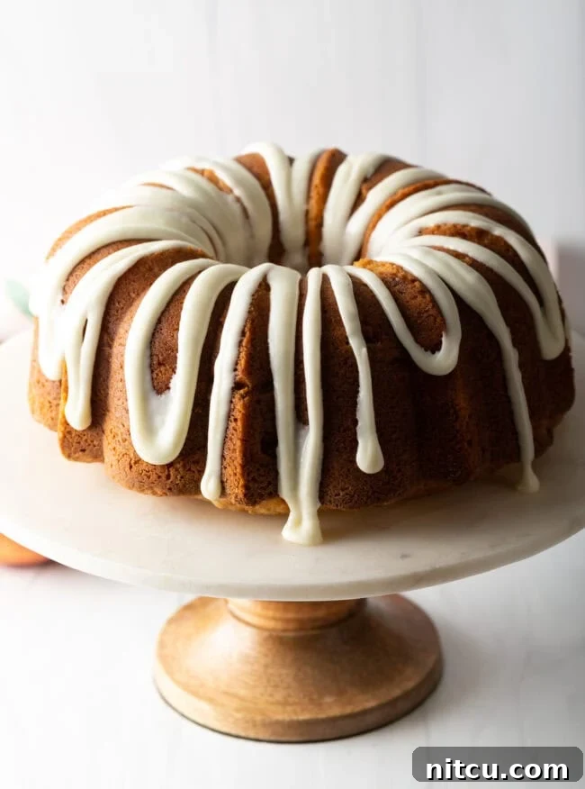 Beautifully glazed peach bundt cake on a white cake stand, ready to be served.
