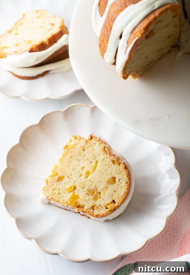 Close-up slice of moist peach bundt cake, revealing tender peach chunks, in a bundt pan.
