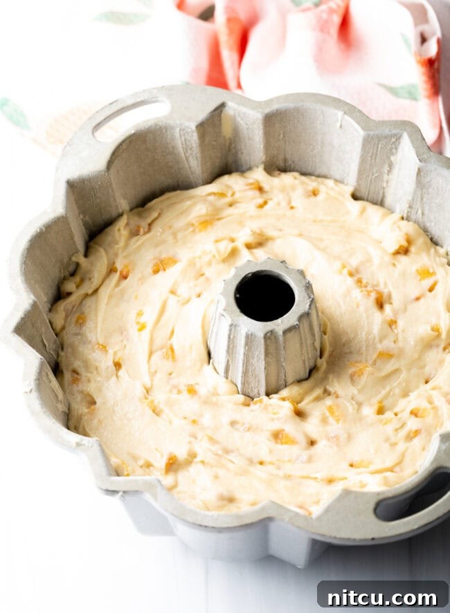 Close-up of peach cake batter, layered with fresh peach pieces, inside a bundt pan before baking.