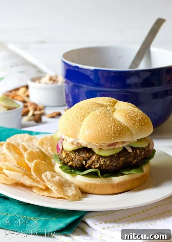 A close-up of a beautifully assembled Mediterranean burger, garnished with fresh dill, served on a plate with chips.