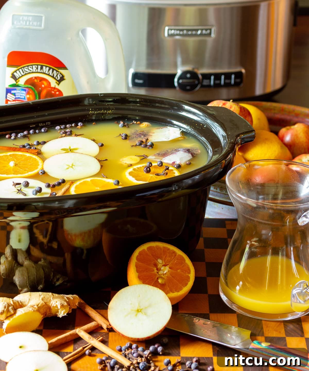 Apple cider wassail recipe in a crock pot with ingredients scattered in front. 