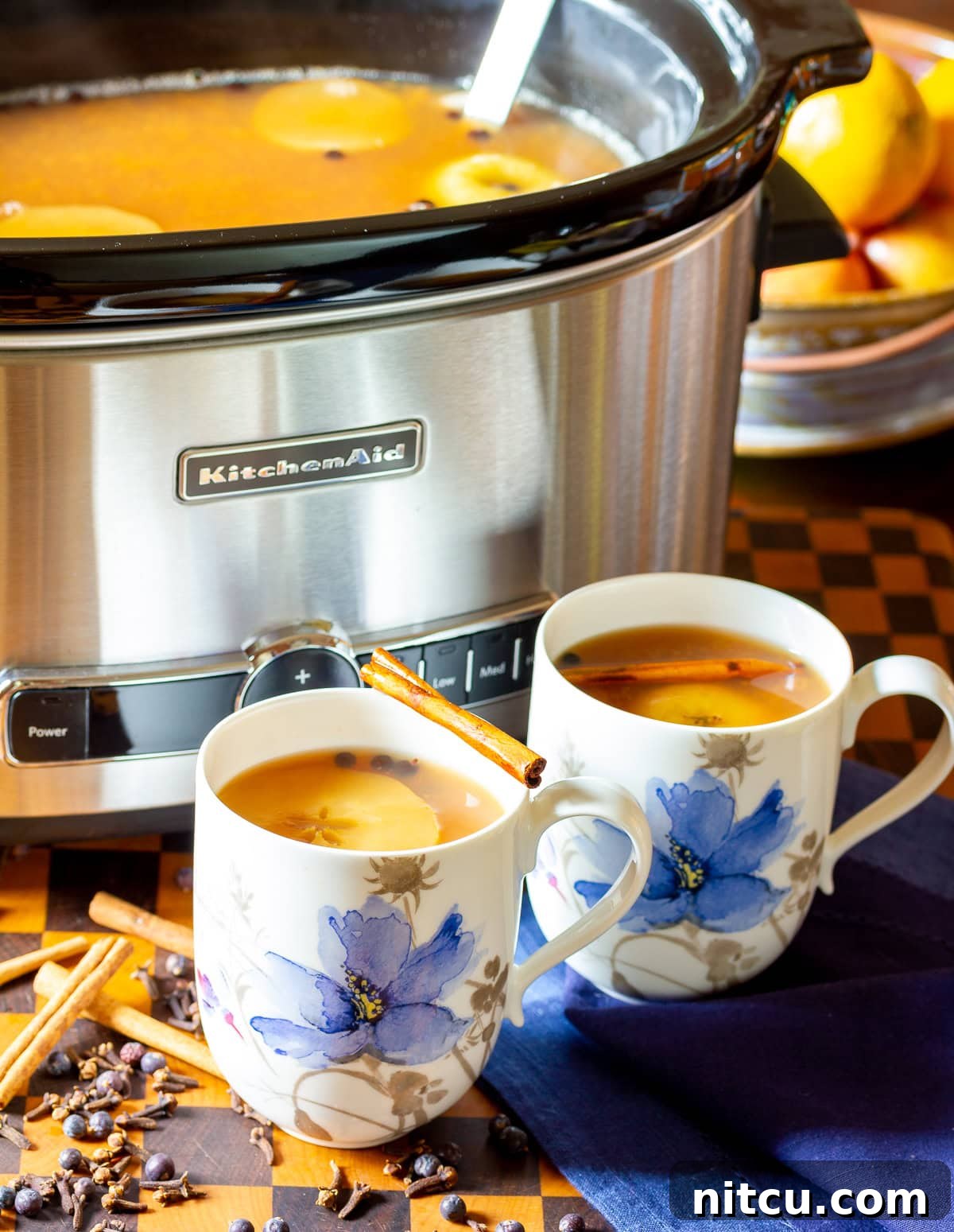 Two mugs with apple cider wassail in them with the crockpot full of more cider in the background. 