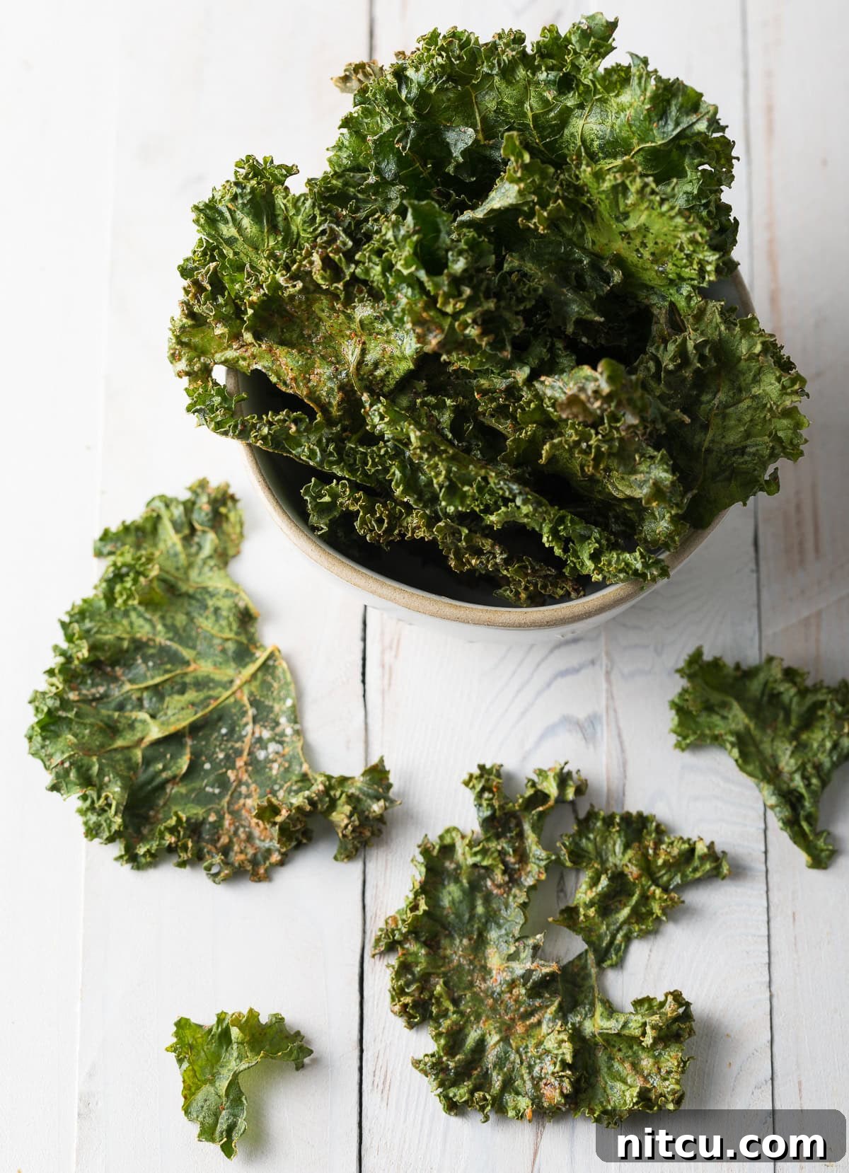 Homemade kale chips in a bowl with a few scattered around.