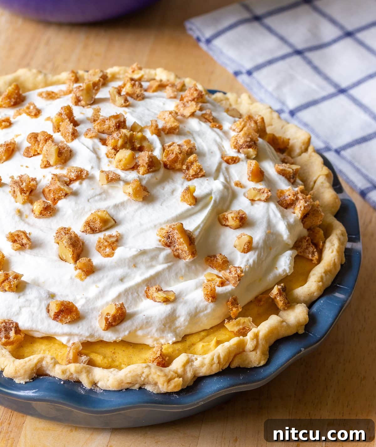 A whole pumpkin dessert with a beautifully crimped pie crust and a generous amount of whipped cream