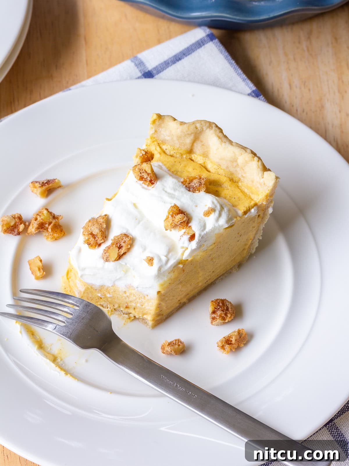 A perfect slice of pumpkin cream pie on a white plate, garnished with candied nuts.