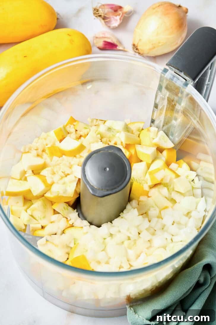 Fresh ingredients for Squash Casserole, including yellow squash, onion, and garlic, prepared for a food processor