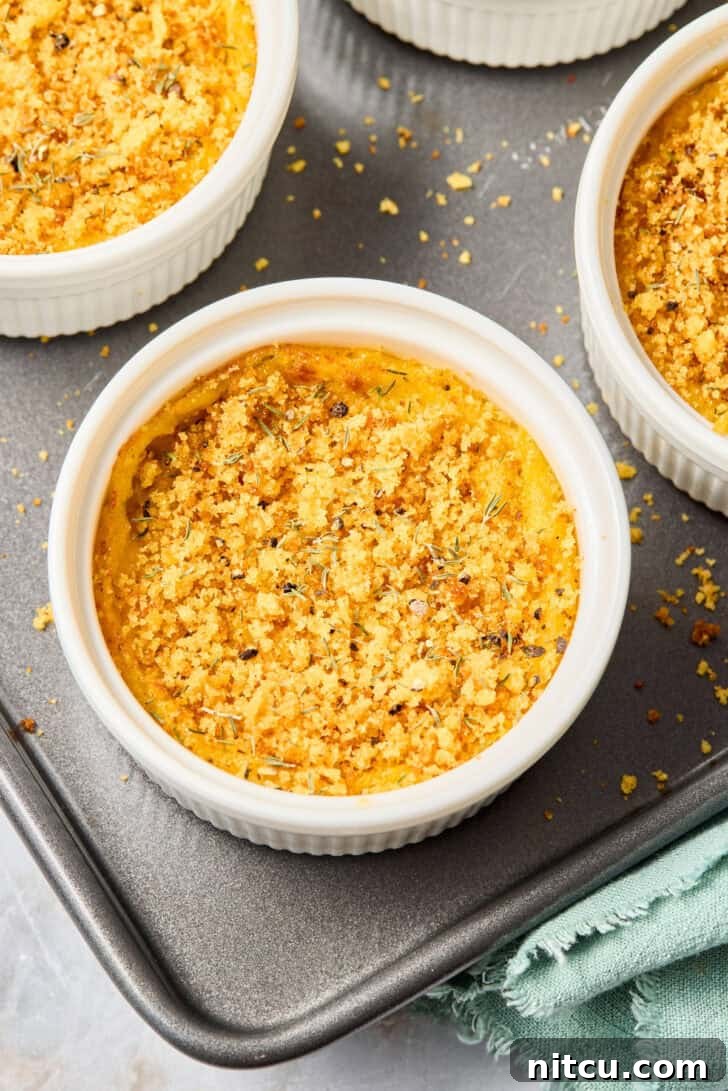 Two ceramic dishes of cheesy squash casserole, freshly baked with a golden top, on a wooden board