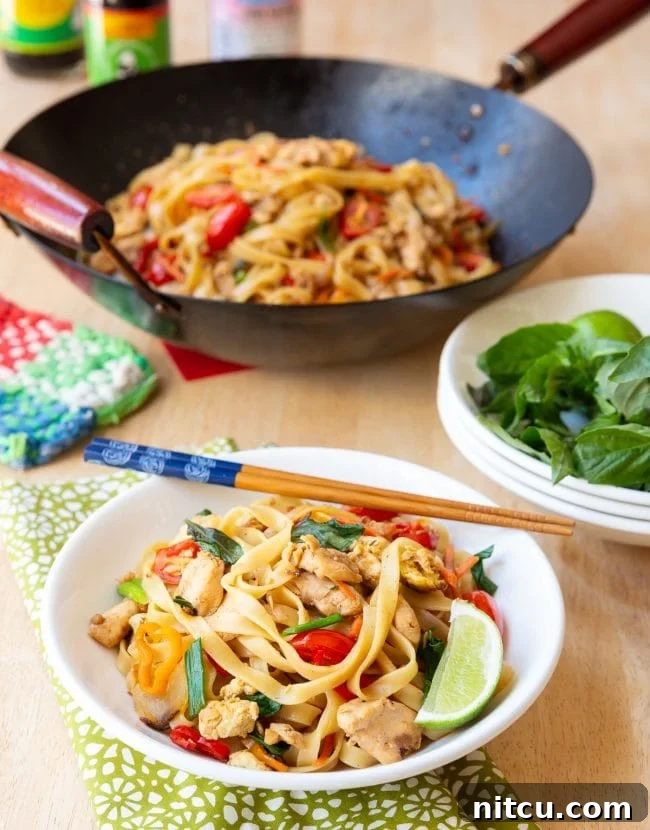 A bowl of delicious Pad Kee Mao (Drunken Noodles) garnished with fresh herbs and a lime wedge, ready to be enjoyed. 