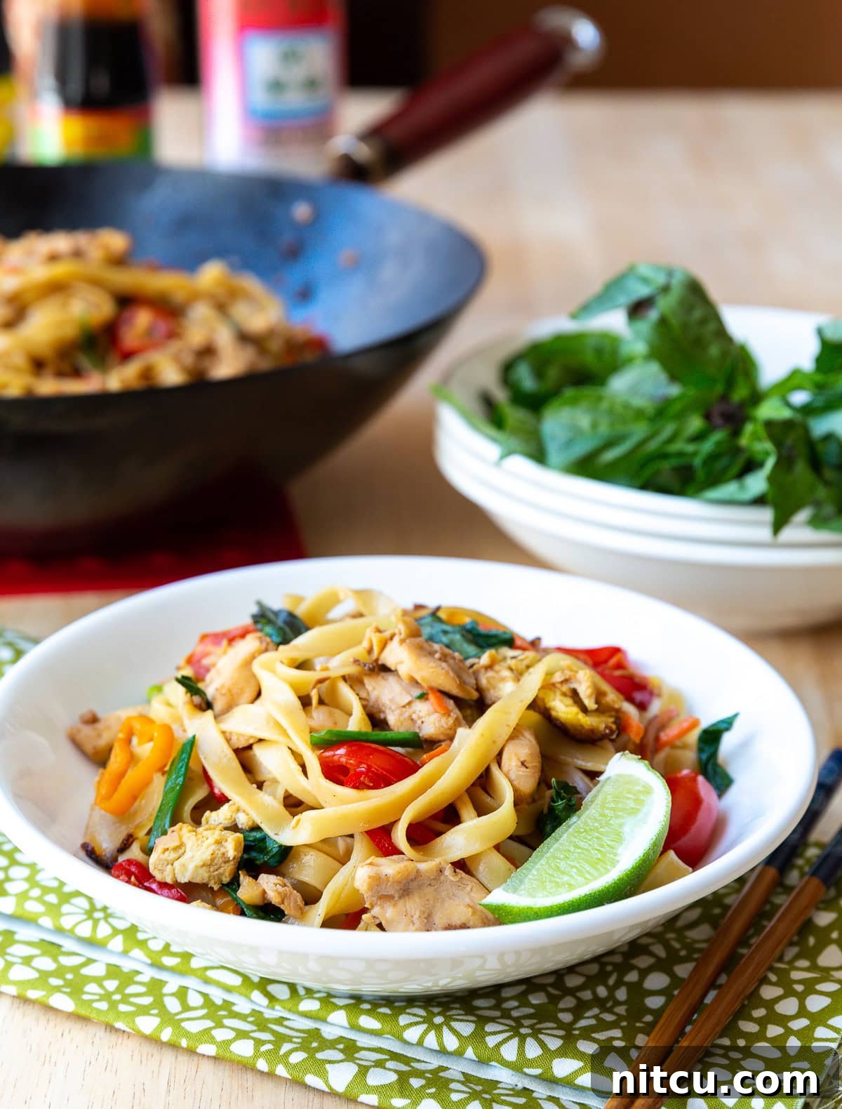 Close-up of freshly cooked Pad Kee Mao in a bowl, with a bright lime wedge and chopsticks ready for serving. 
