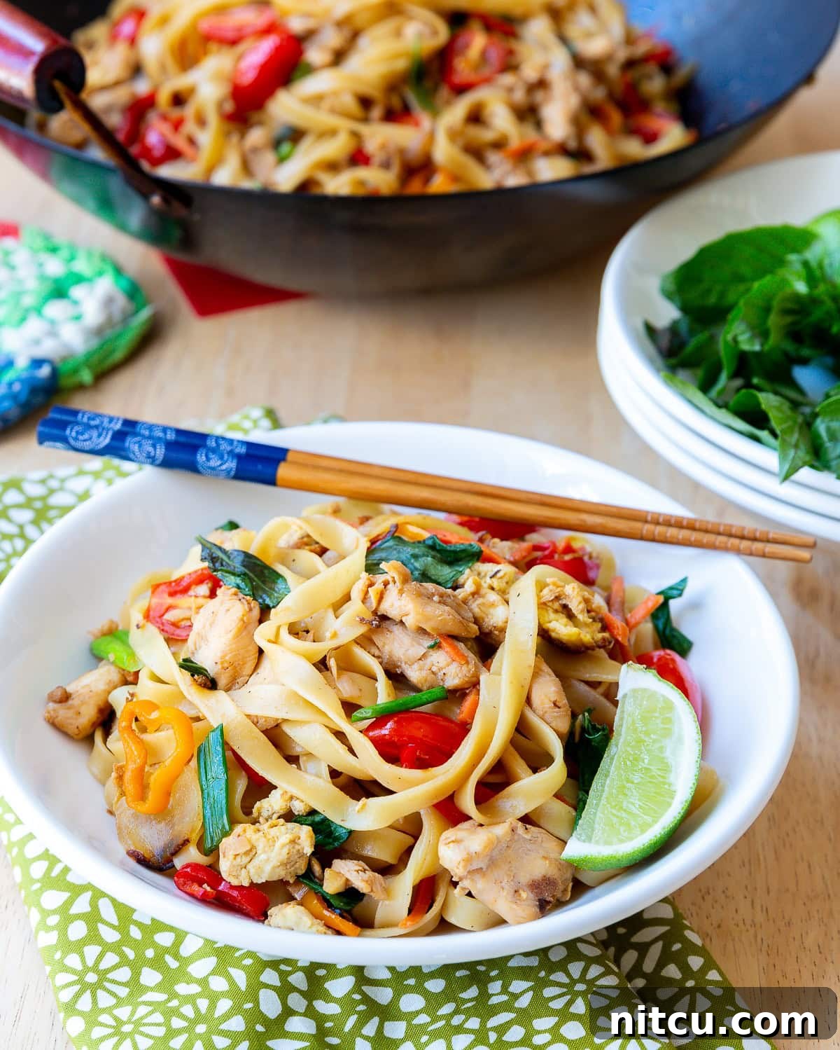 A beautifully plated bowl of Pad Kee Mao, served with fresh lime and chopsticks, highlighting its vibrant colors and textures.