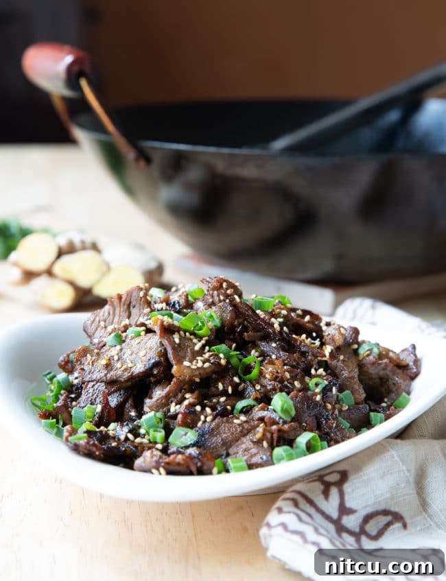 Korean beef bulgogi served in a white bowl with a black wok in the background.