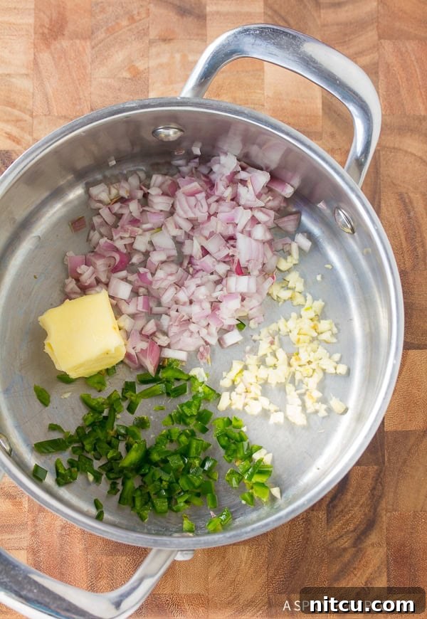 Diced jalapenos, shallots, garlic, and butter being sauteed in a pot, releasing fragrant aromas.